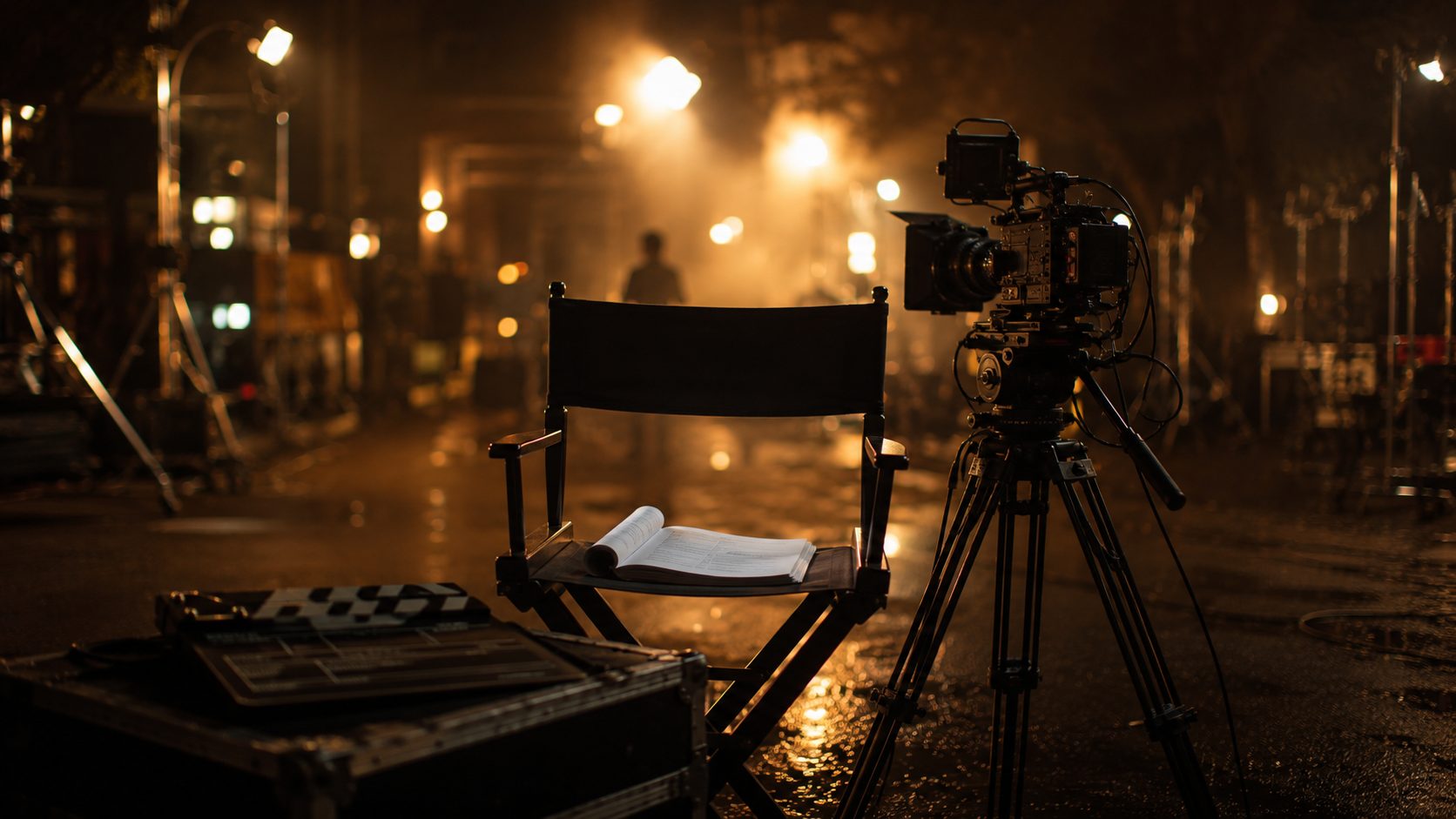 Nächtliches Filmset mit Regiestuhl, aufgeschlagenem Drehbuch und Kinokamera im goldenen Scheinwerferlicht
